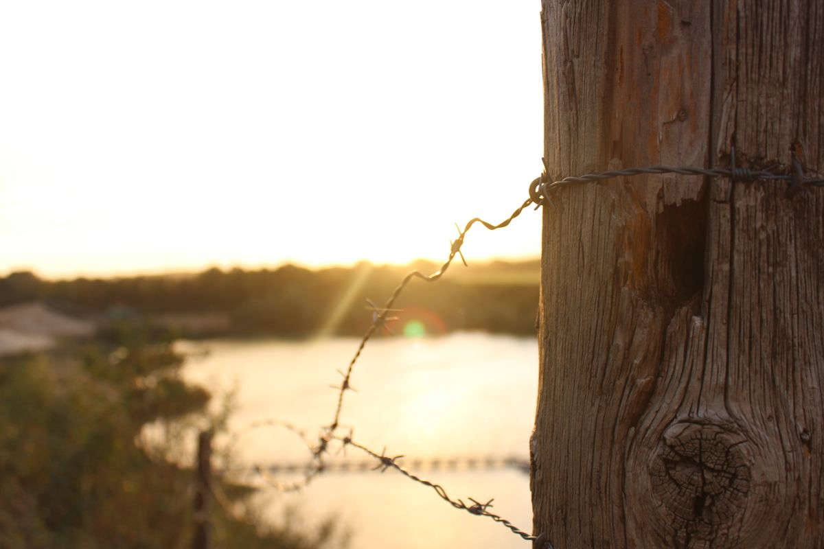 Close-up of barbed wire on a wooden post with a warm sunset in the background.