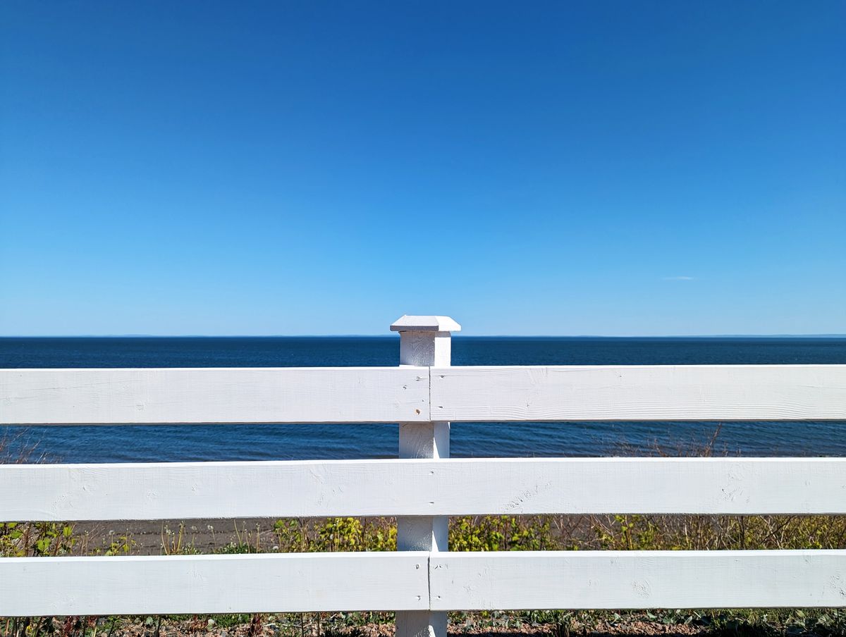 Serene view of a white wooden fence facing the ocean under a clear blue sky in summer.