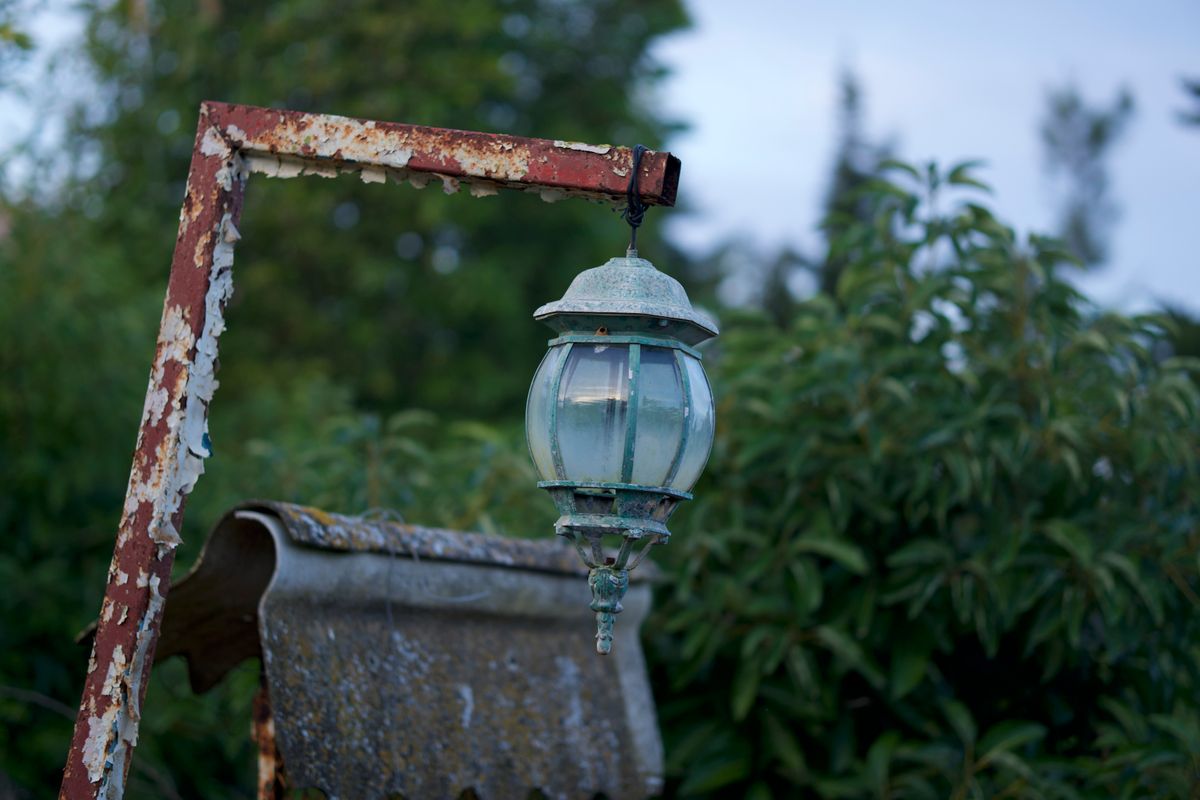 Close-up of a rusty vintage lantern with greenery in the background, evoking an antique garden charm.