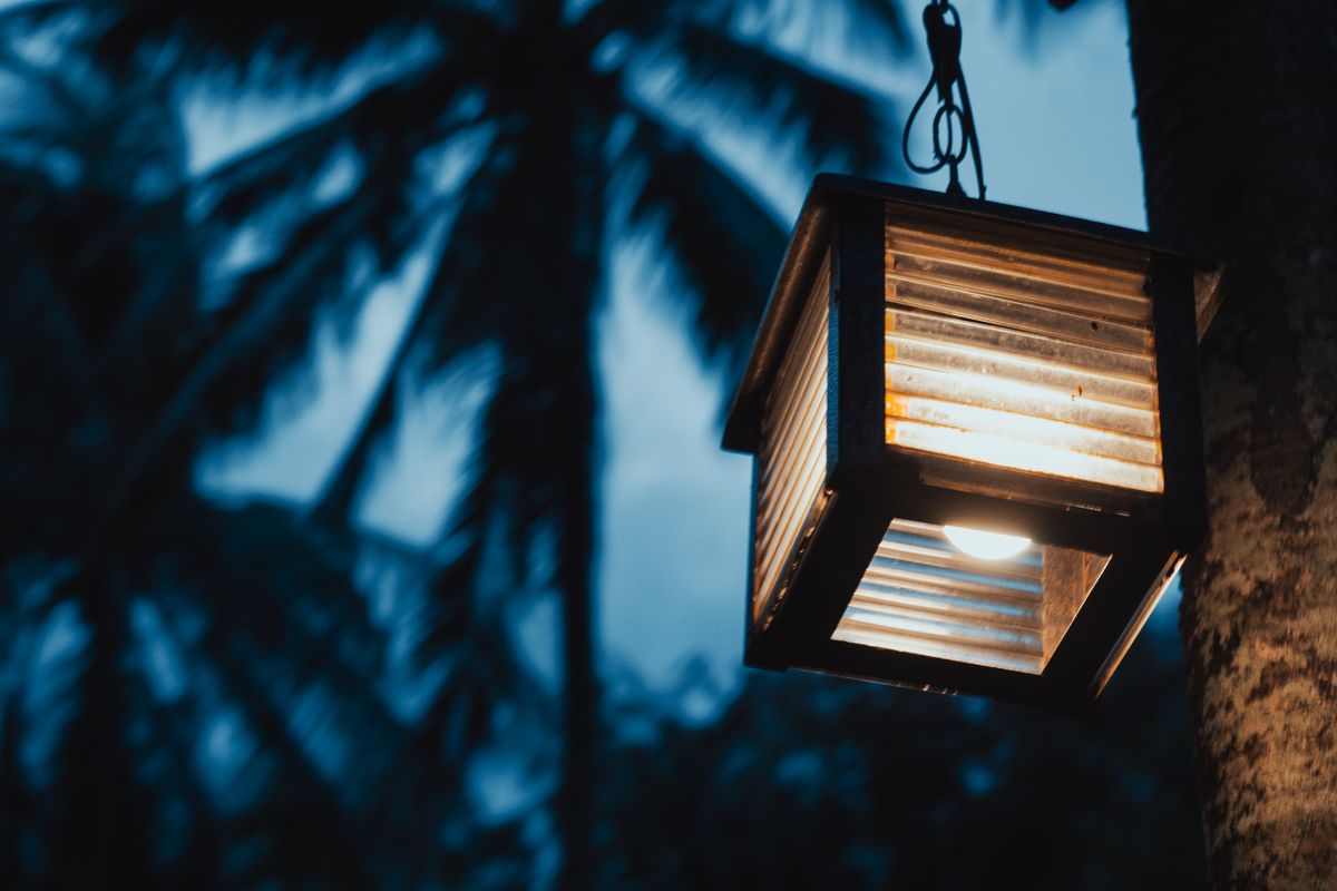 A warm glowing lantern hangs in front of silhouetted palm trees at twilight in Malay, Philippines.