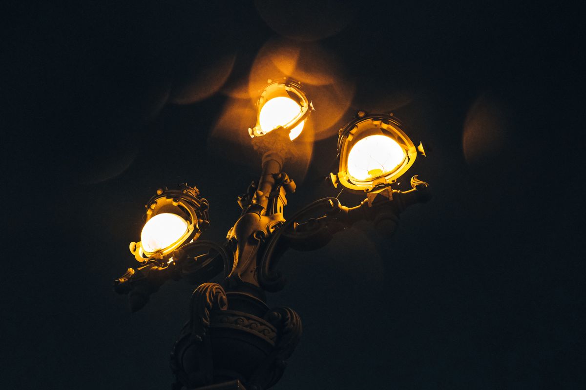 A close-up of a vintage street lamp illuminating the night sky with warm glowing lights.