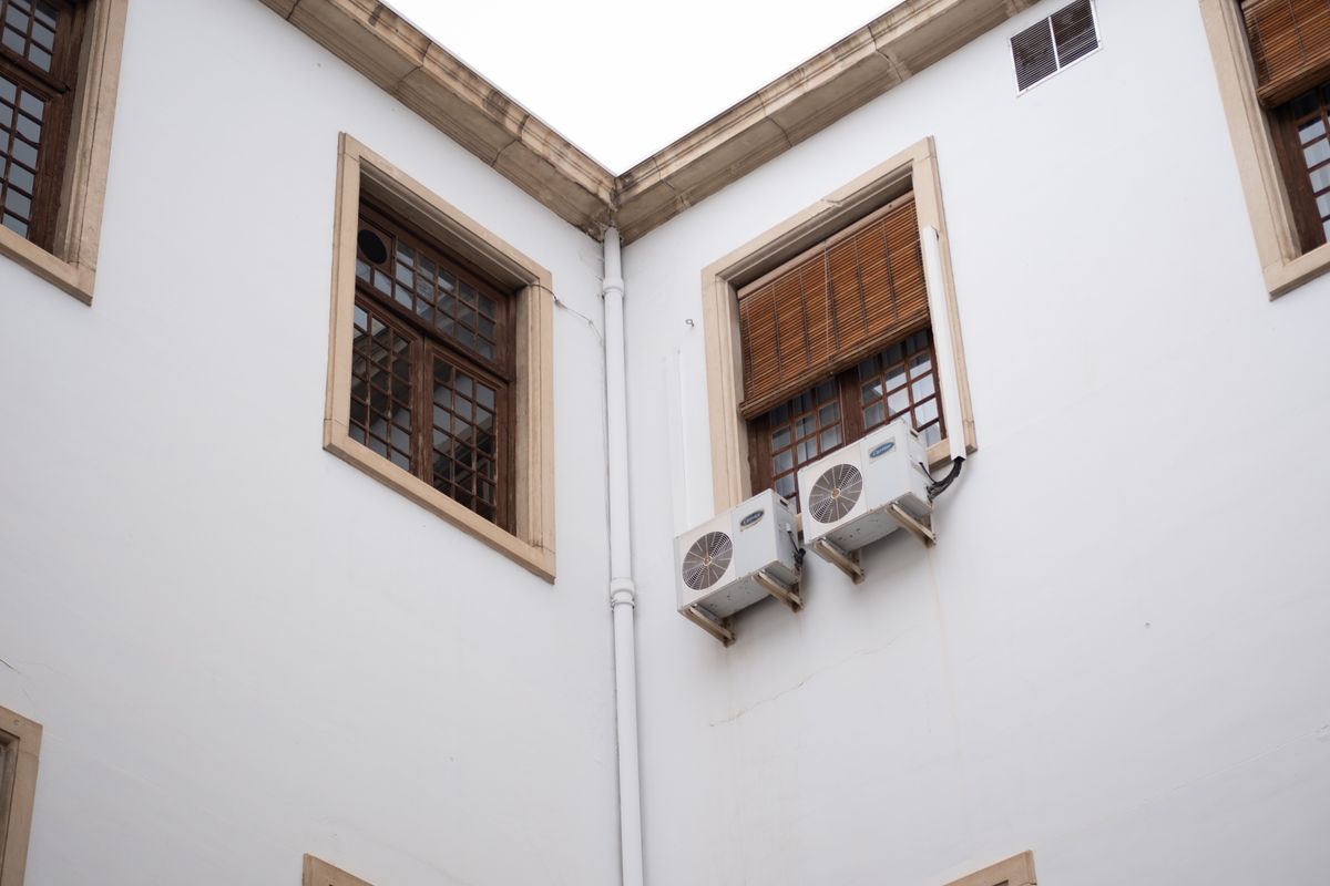White building facade with wooden window shades and air conditioning units.