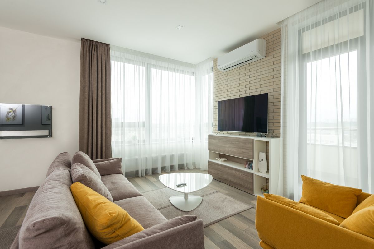 Soft comfortable sofa with cushions and armchair placed in front of TV hanging on brick wall in spacious living room of modern apartment