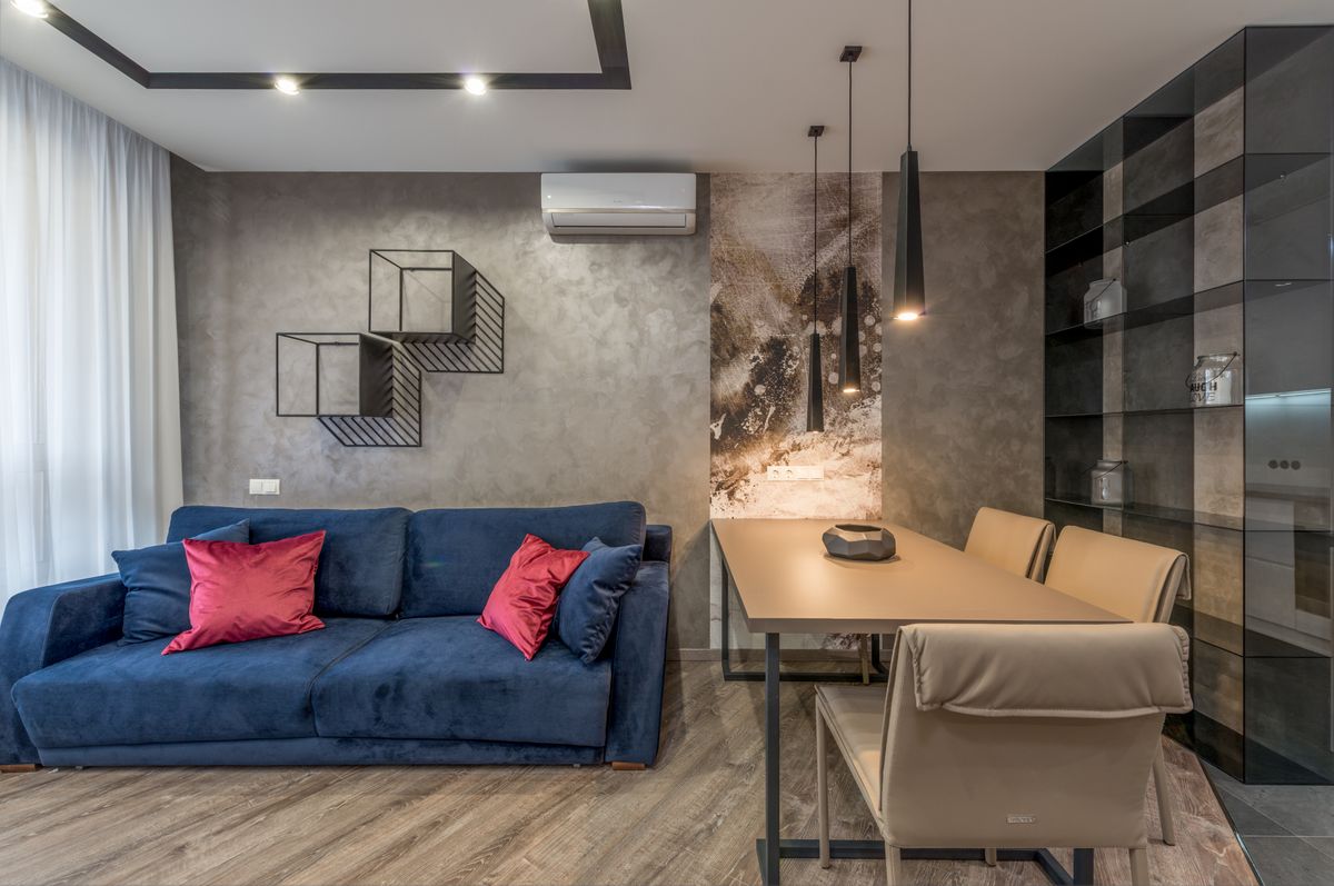 Interior of contemporary spacious living room furnished with soft sofa with cushions placed near dining table with chairs