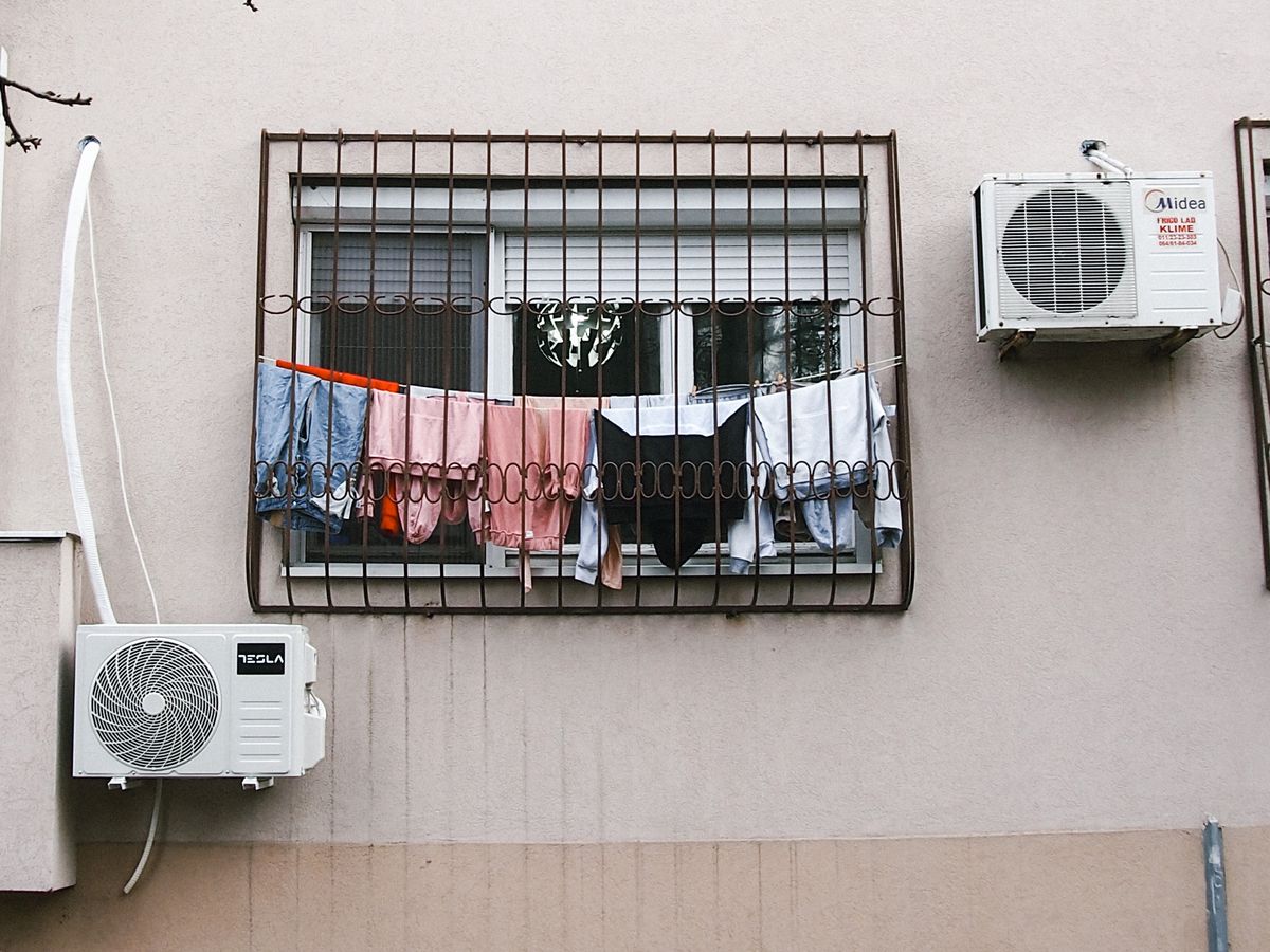 Clothes hanging to dry on a barred window with air conditioners in an urban setting.