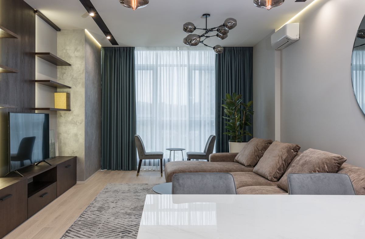 Comfy sofa with pillow and dining table with chairs placed in front of TV set placed on wooden cabinet in modern living room
