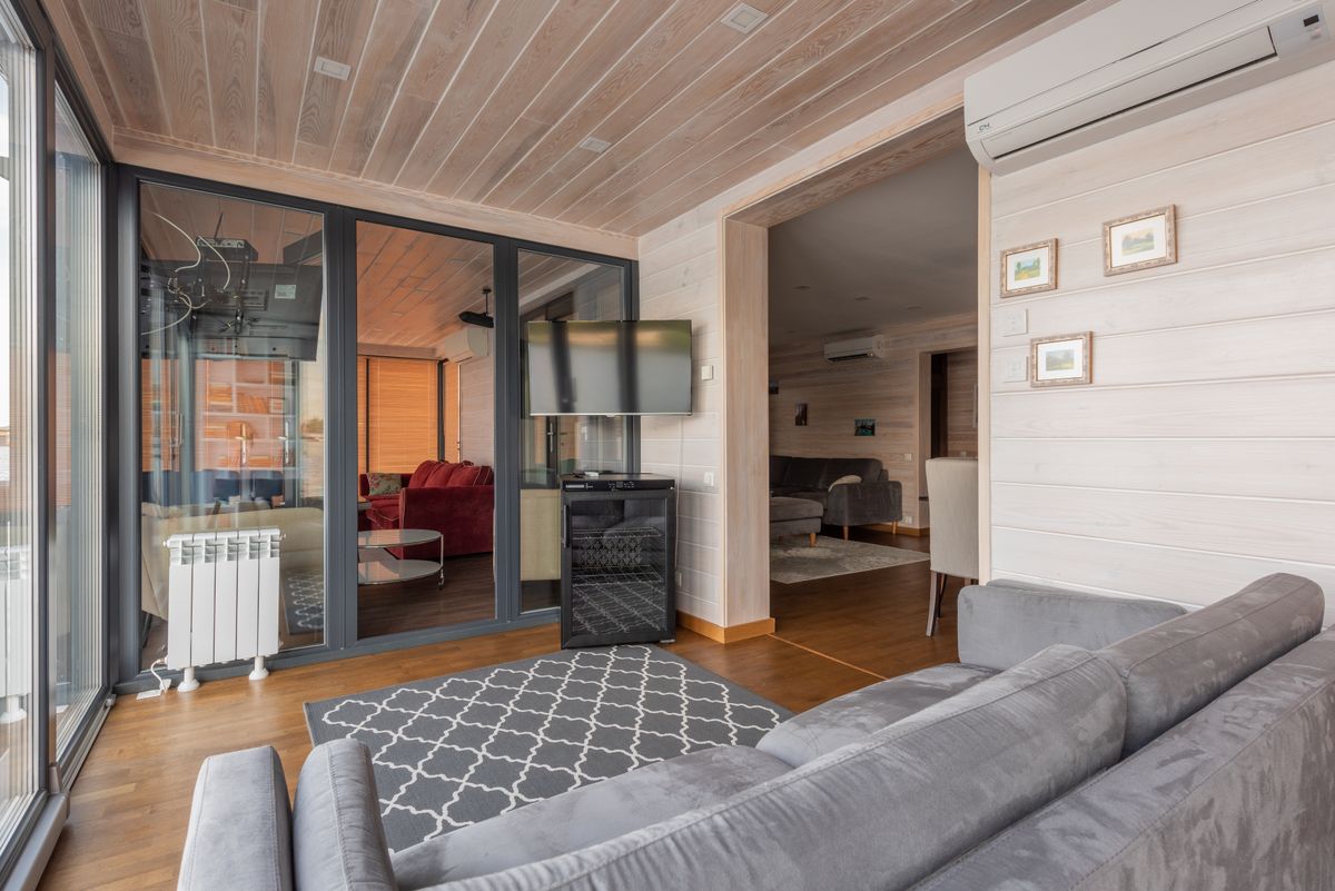 Spacious modern living room featuring glass doors, wooden ceilings, and elegant furnishings.