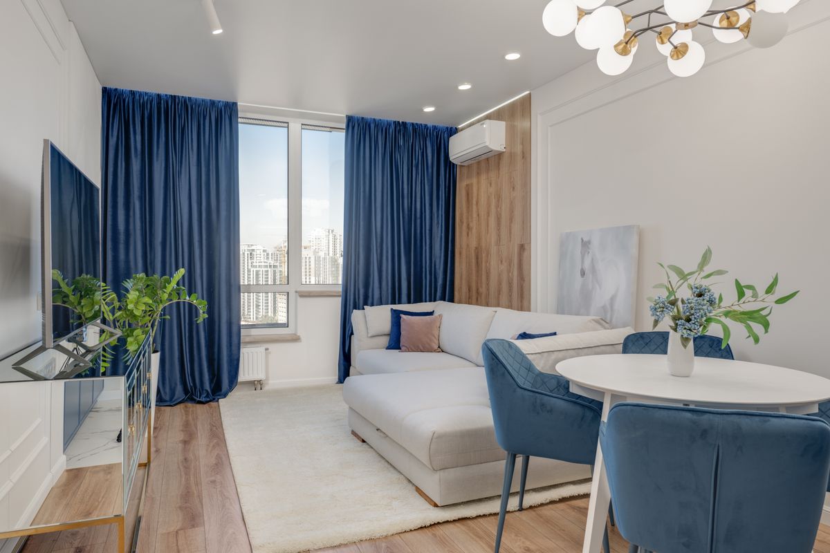 Bright living room with blue curtains, plants, and modern furniture.
