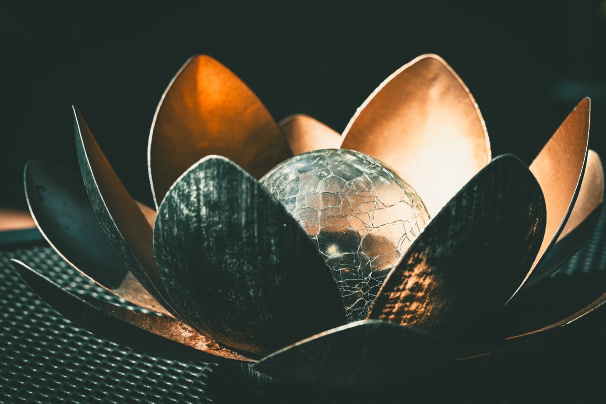 Metal lotus sculpture with a cracked glass sphere, capturing a dramatic play of light and shadow.