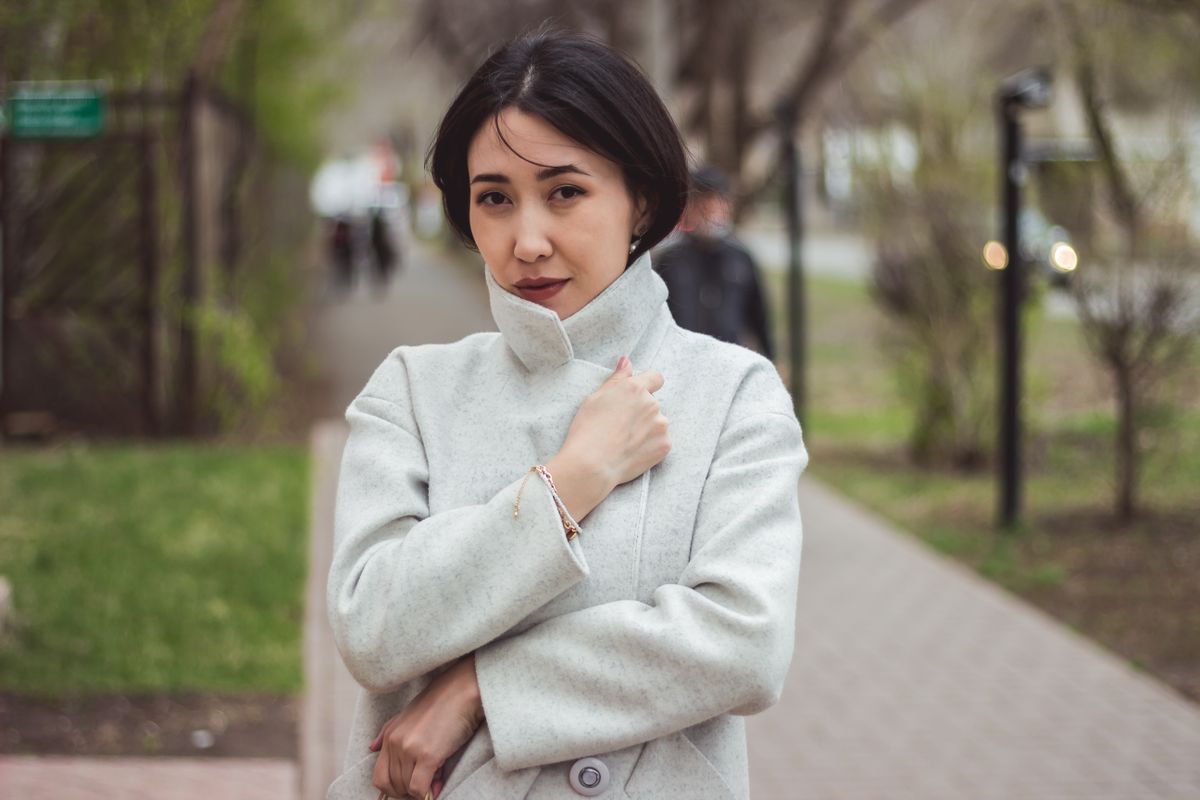 Portrait of an elegant woman in a light coat on a city sidewalk, showcasing urban fashion.