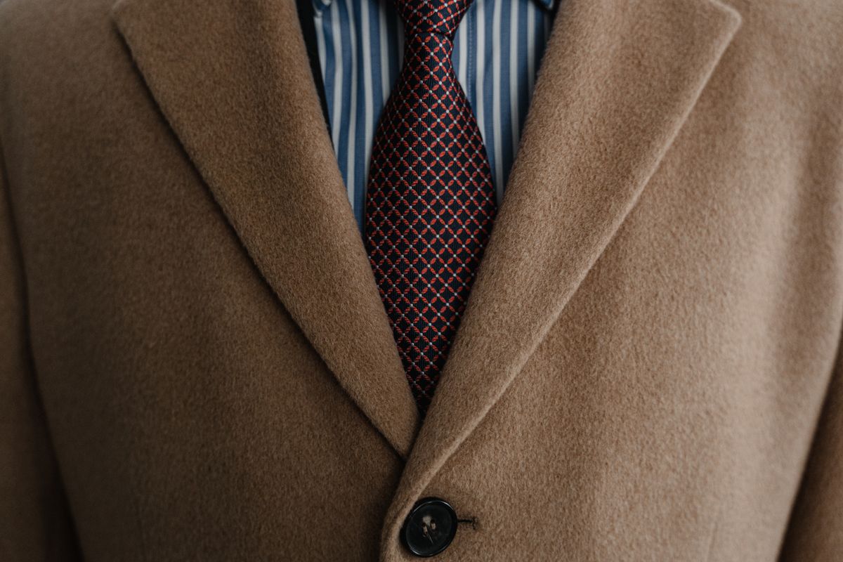 Close-up of a sophisticated brown wool coat over a striped shirt and patterned tie.
