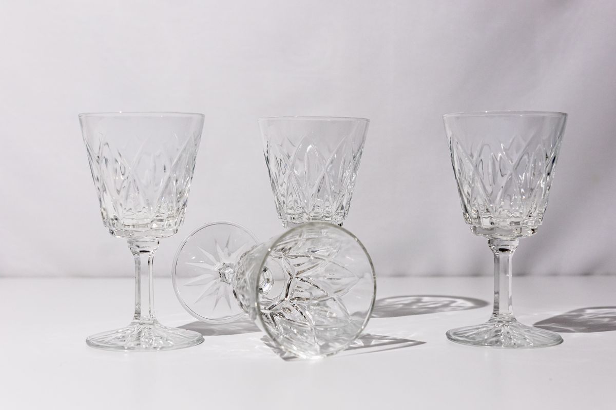 Four crystal wine glasses arranged on a white surface with shadows, showcasing elegance and luxury.