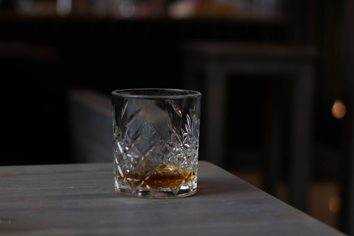 Cut glass with aromatic cognac on bottom placed on wooden table in dark living room