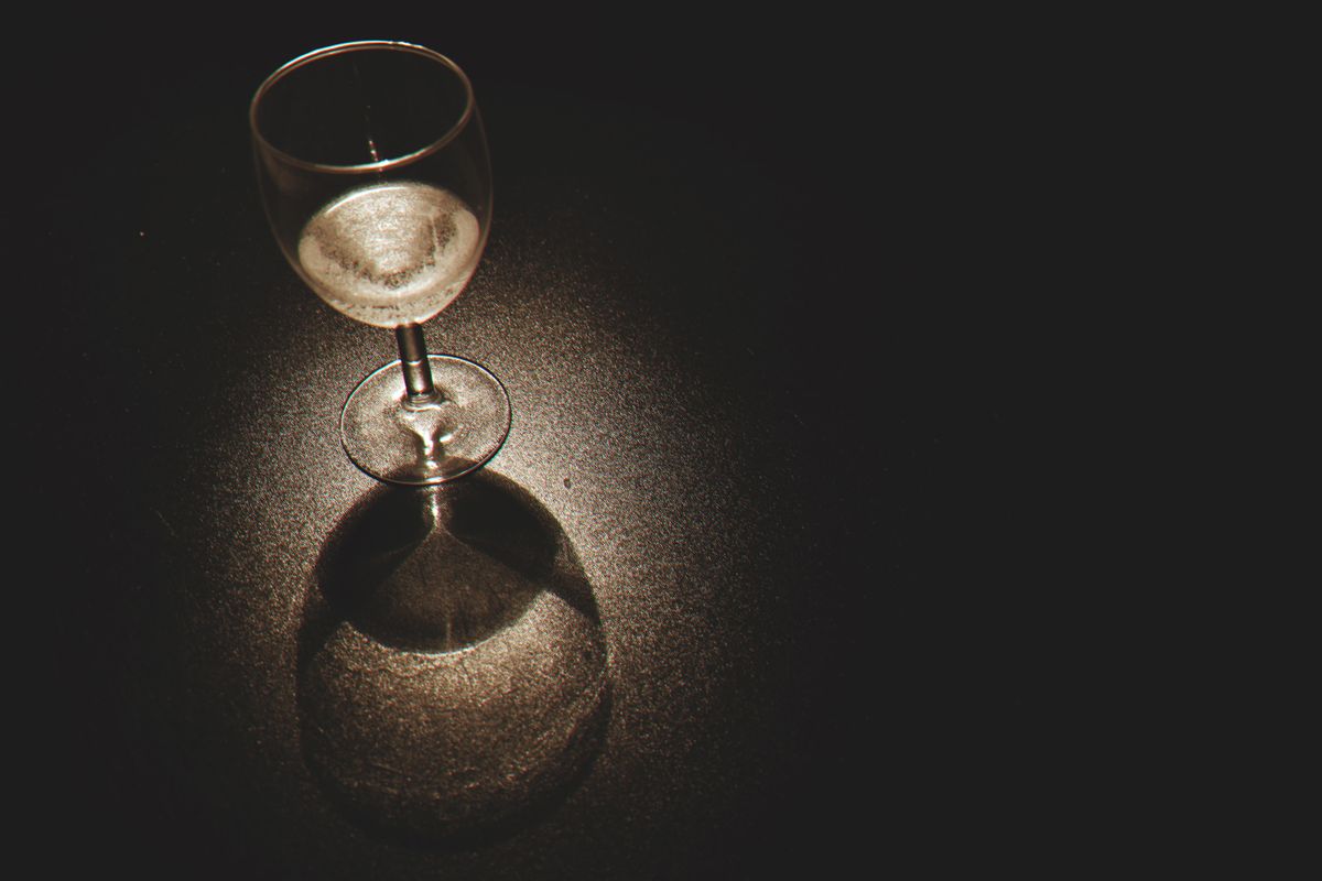 A crystal wine glass casting shadows with light reflections on a dark surface.
