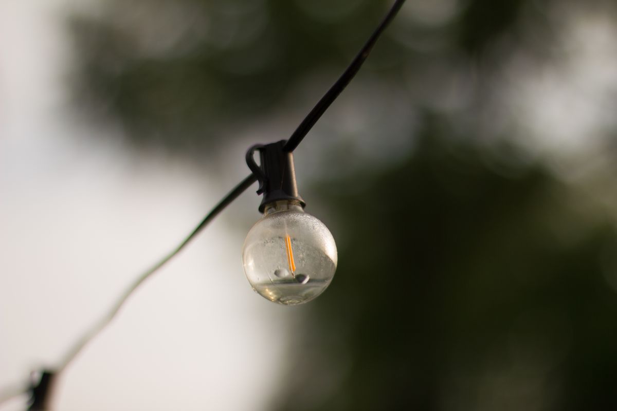 A hanging light bulb with a blurred green background, capturing the essence of outdoor lighting.