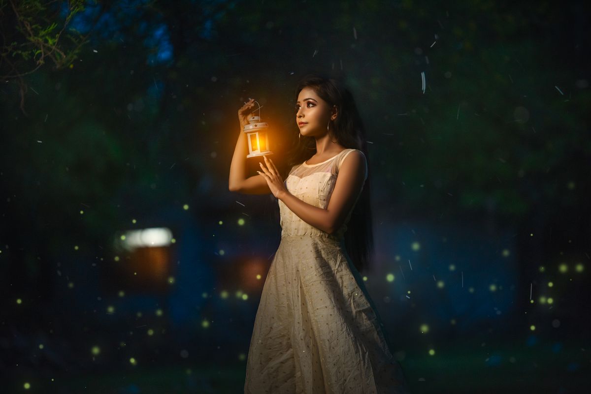 A woman in a white dress holds a glowing lantern, creating a magical ambiance at night.