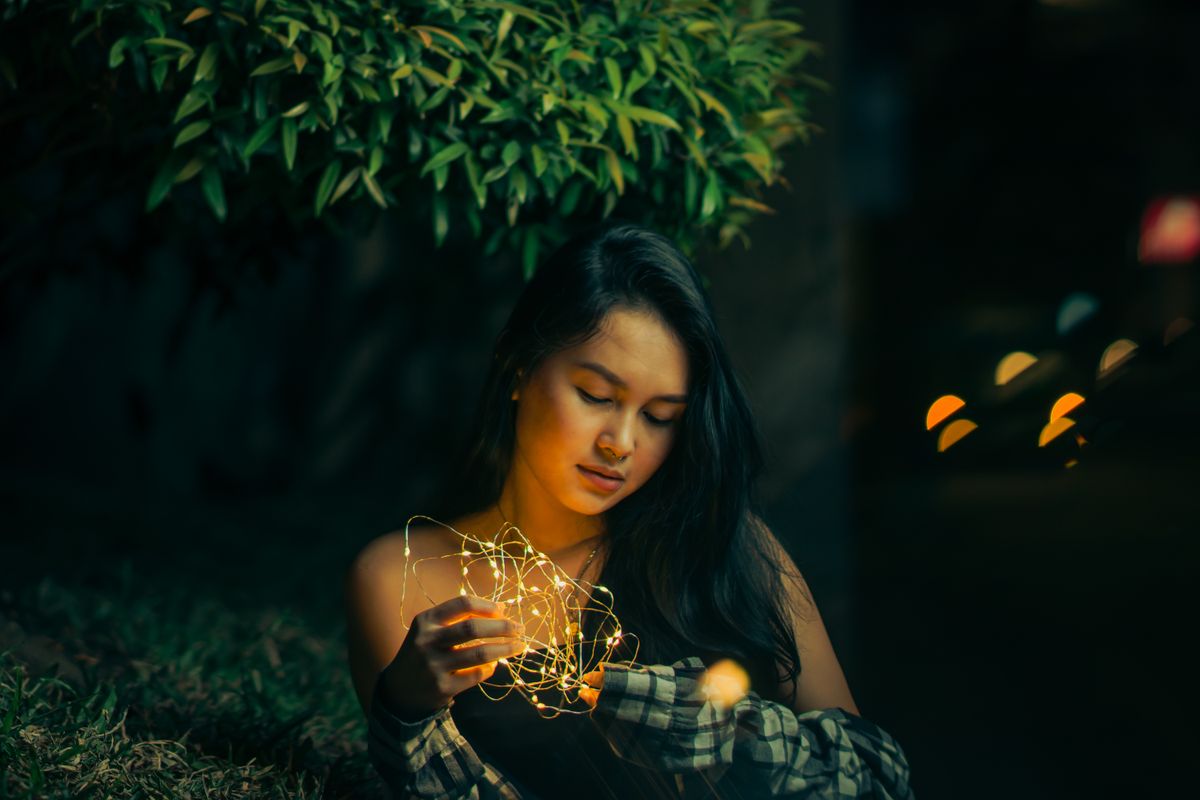 A young woman holding string lights in a serene night setting, showcasing a calm and enchanting mood.