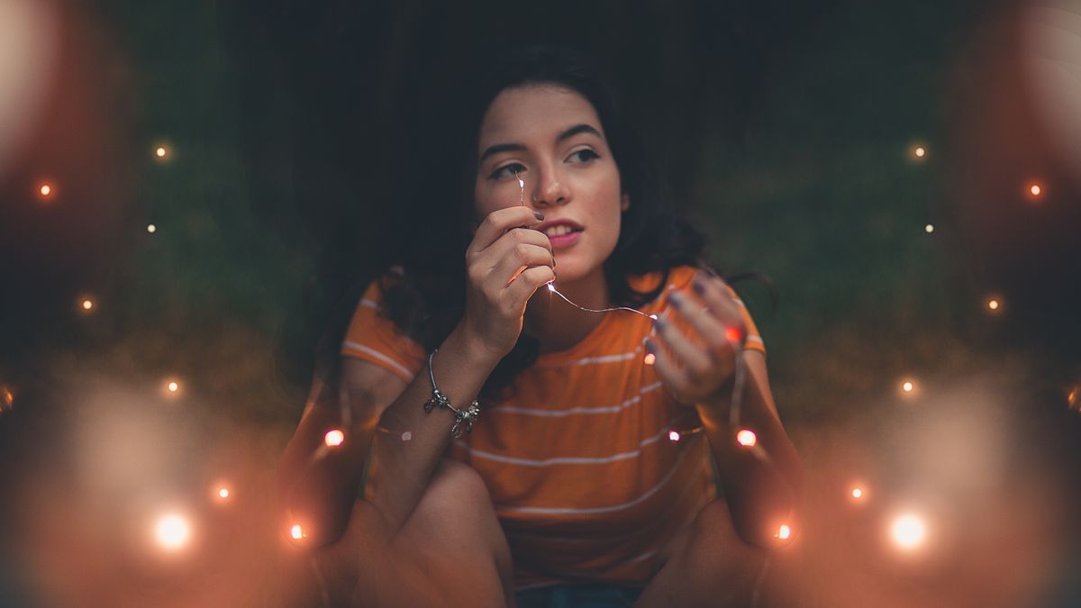 Captivating portrait of a woman with glowing string lights outdoors at night.