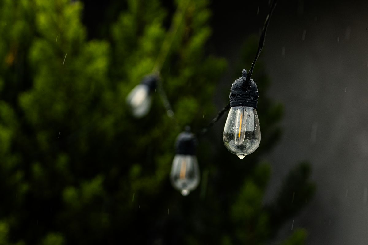 Close-up of raindrops on string lights with blurred green background, creating a moody outdoor ambiance.