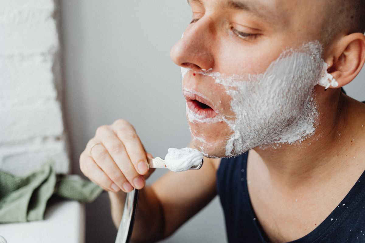 Man applying shaving cream on face with brush for morning grooming routine.