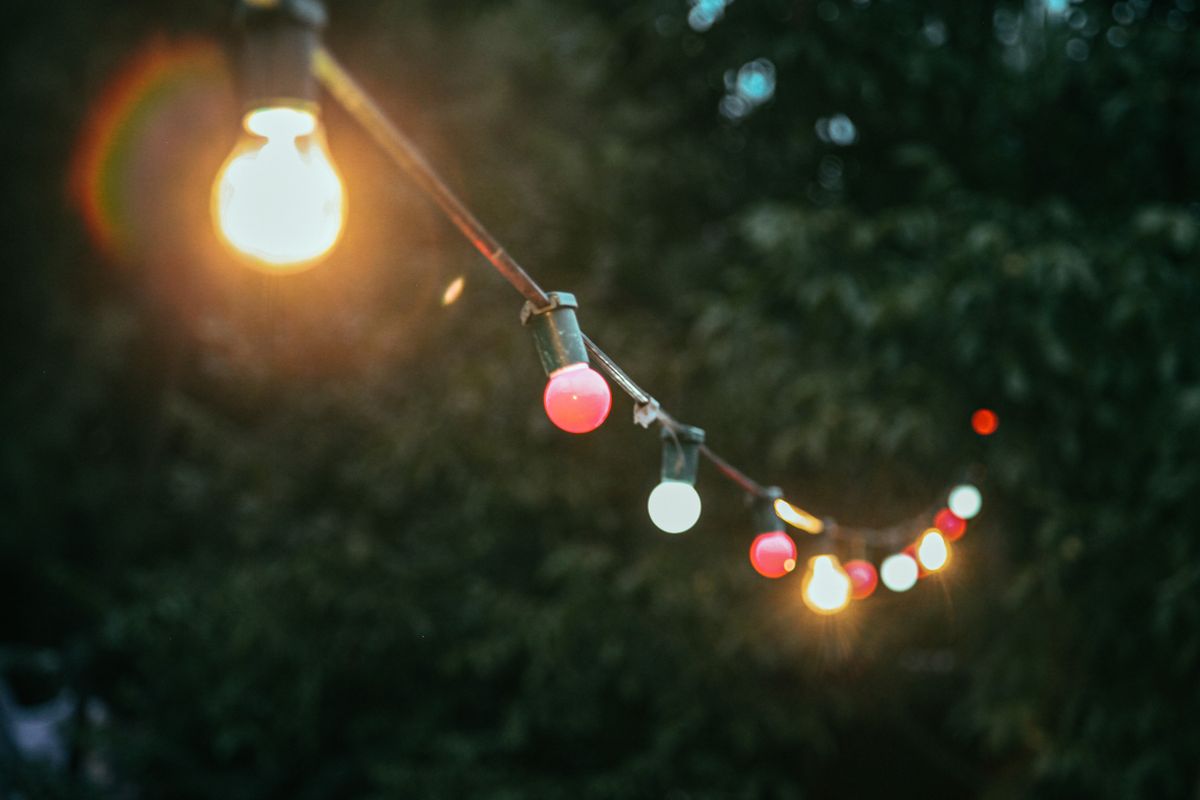 Colorful string lights illuminate an outdoor setting with a blurred background of foliage.