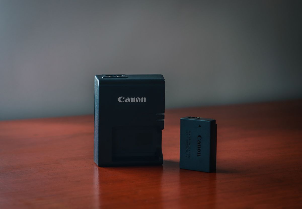 Close-up of a Canon battery and charger on a wooden table with a blurred background.