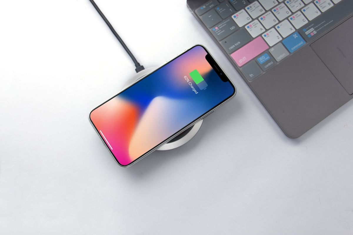 Smartphone wirelessly charging on a pad next to a laptop keyboard on a clean desk.