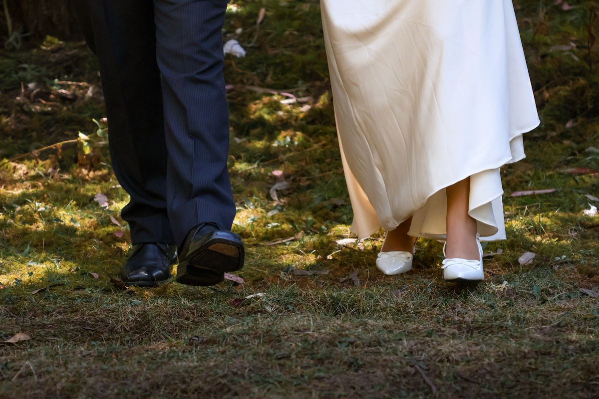 Close-up of bride and groom's feet walking on a forest path, elegant wedding scene.