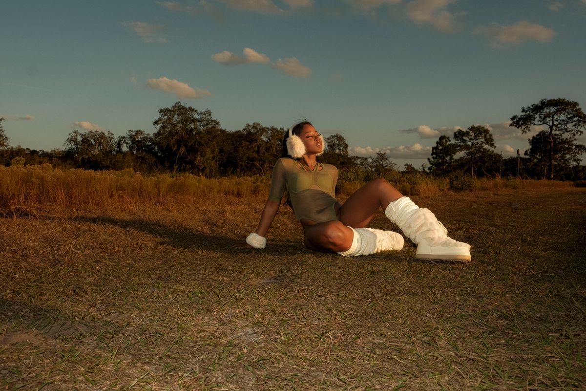 Stylish woman relaxing outdoors wearing earmuffs and boots, front view.