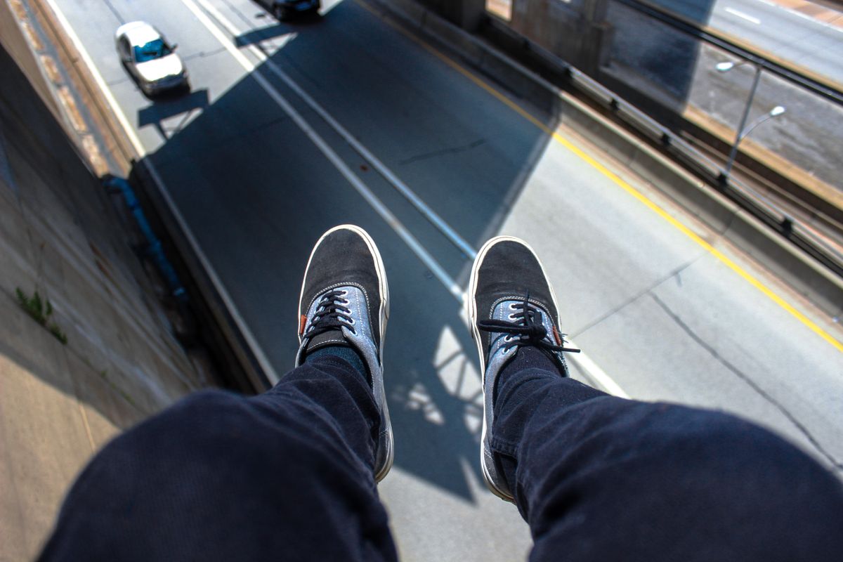 A daring perspective of feet in sneakers dangling over a busy urban road, viewed from above.