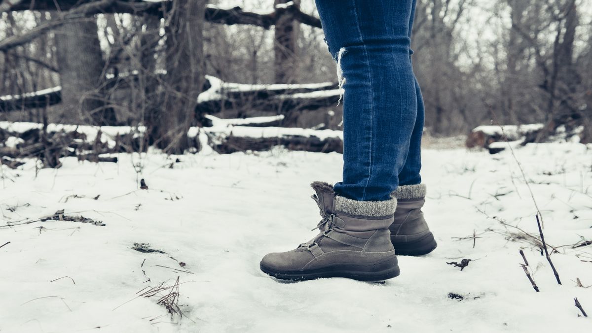Close-up of person wearing winter boots and blue jeans on a snowy forest path.