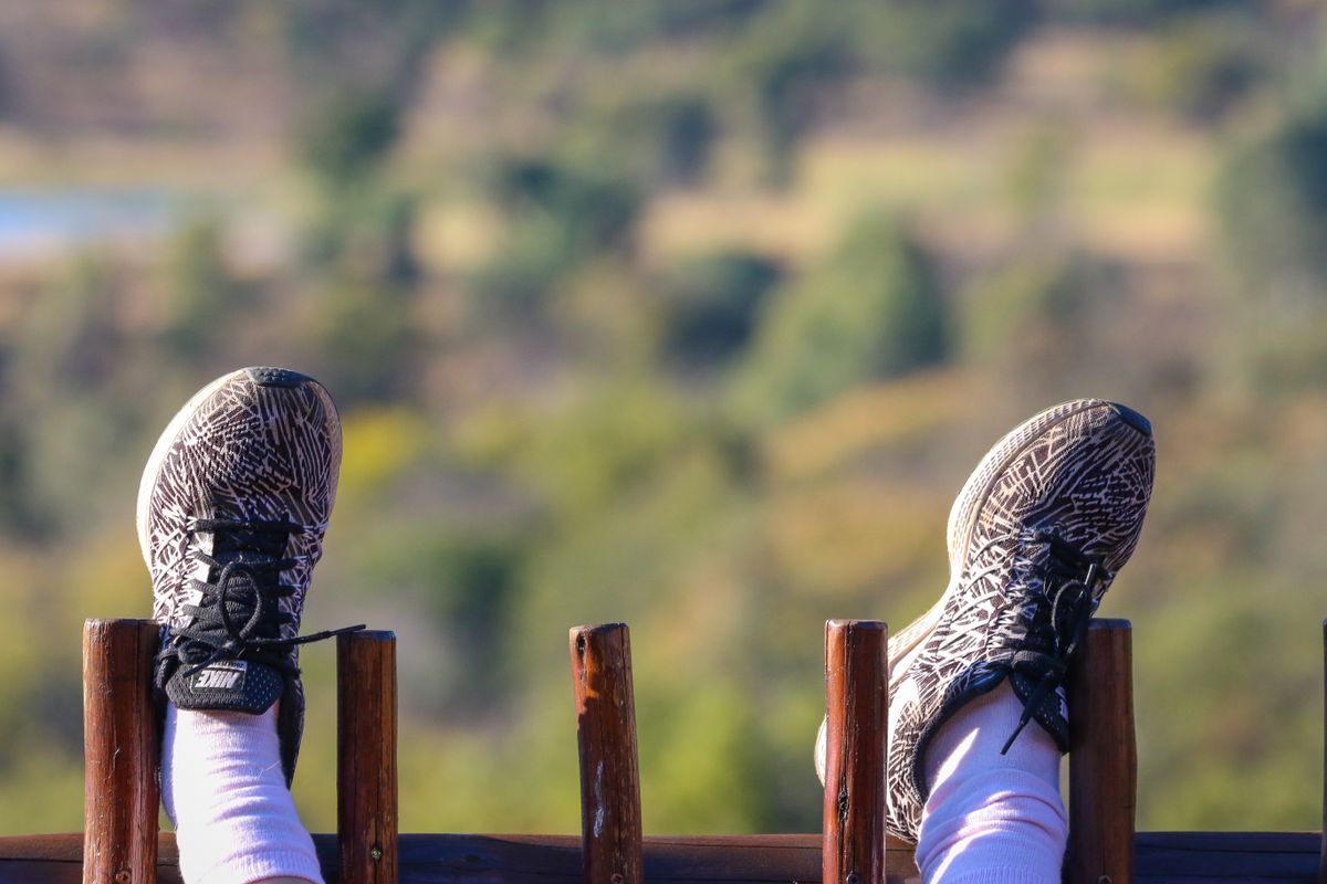 A person wearing sneakers relaxes outdoors with feet on a wooden fence, enjoying a sunny day.