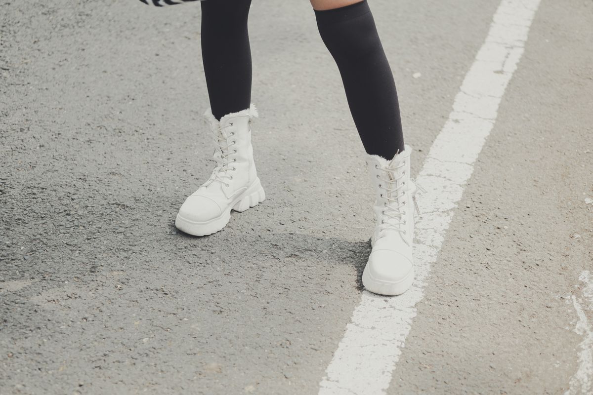 Close-up of stylish white boots on a city road, featuring black knee-high socks.