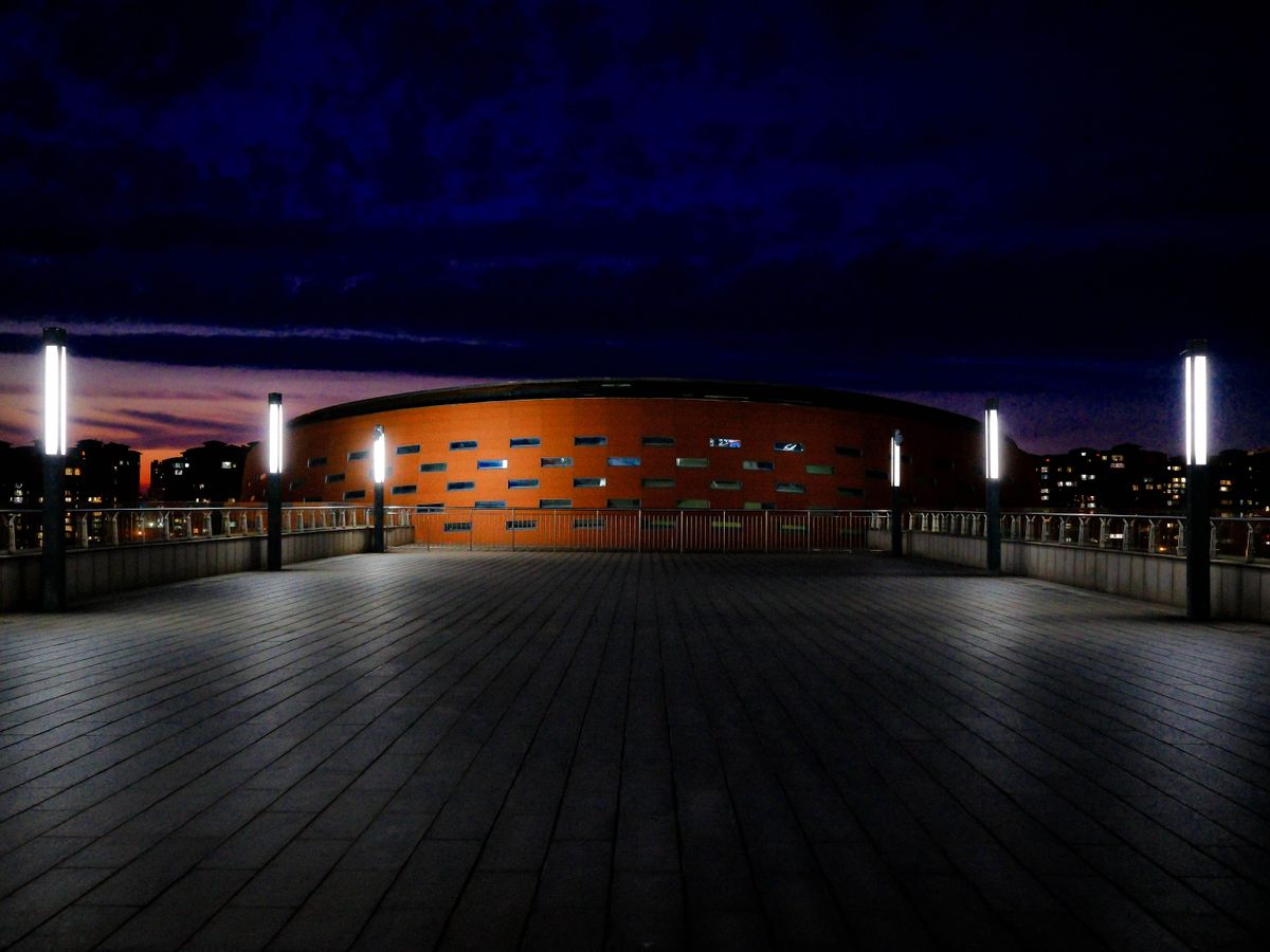 An illuminated modern building and plaza at night under a deep blue sky.