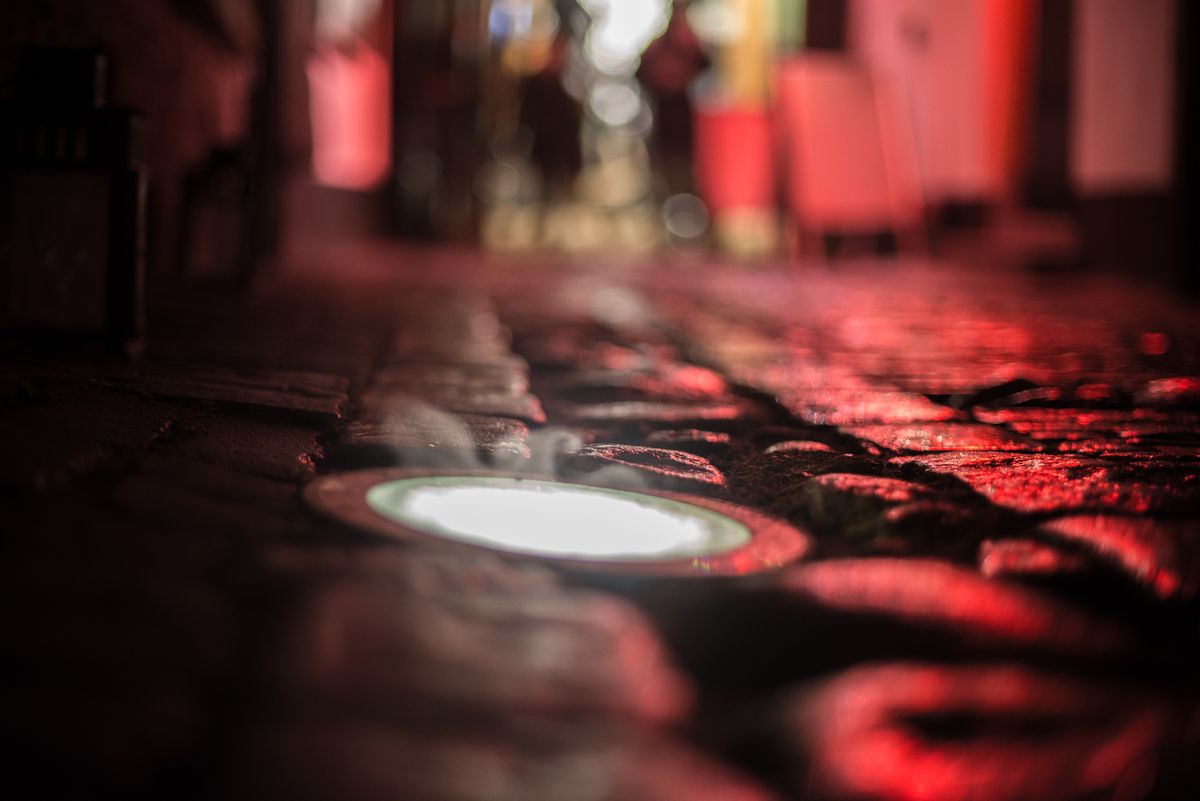 Blurred view of a cobblestone street illuminated by red lights, creating a moody night atmosphere.