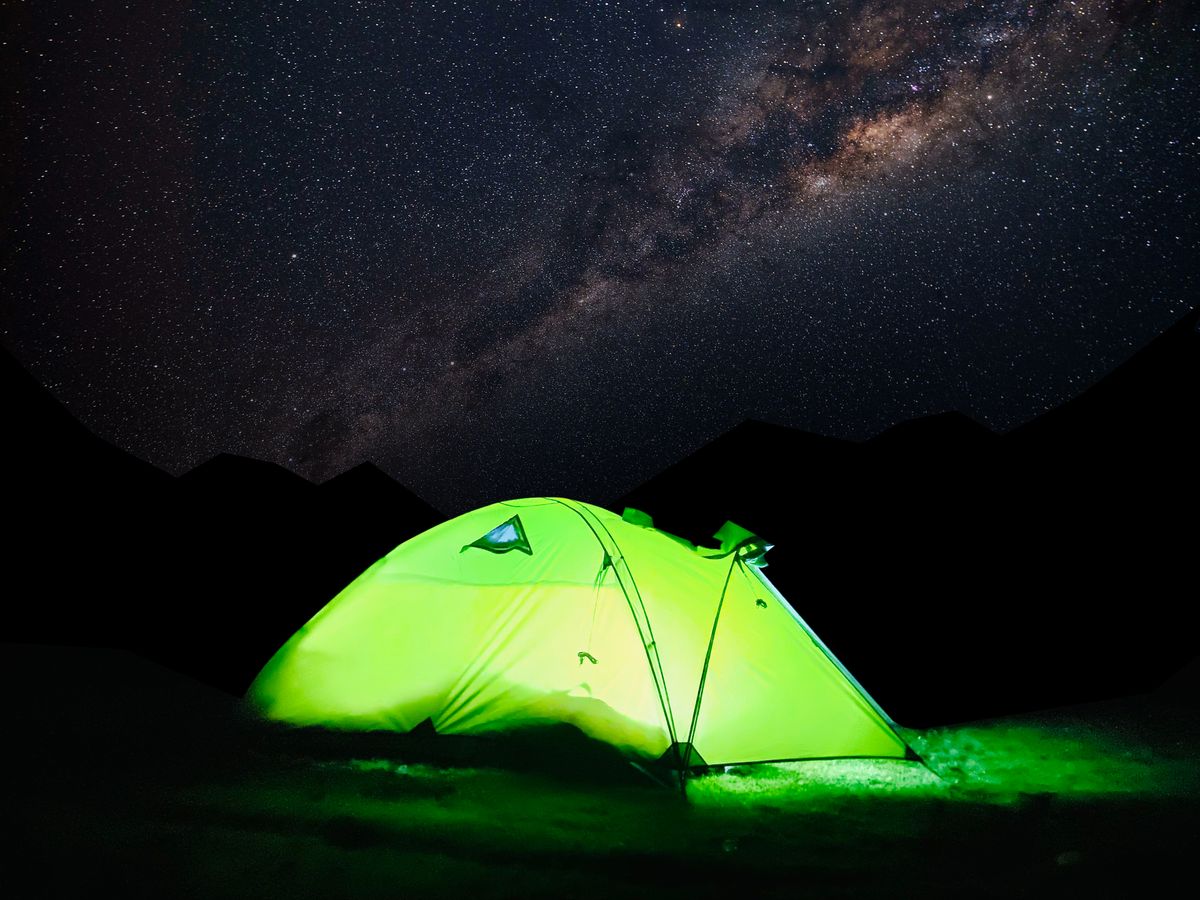 A glowing green tent set against a starry night sky with the Milky Way.