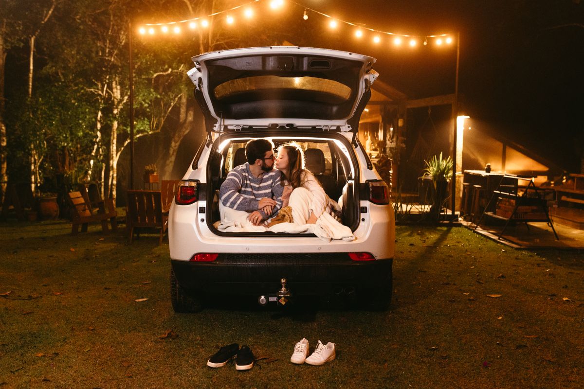 A couple sharing a kiss in the trunk of a car under outdoor lights at night.