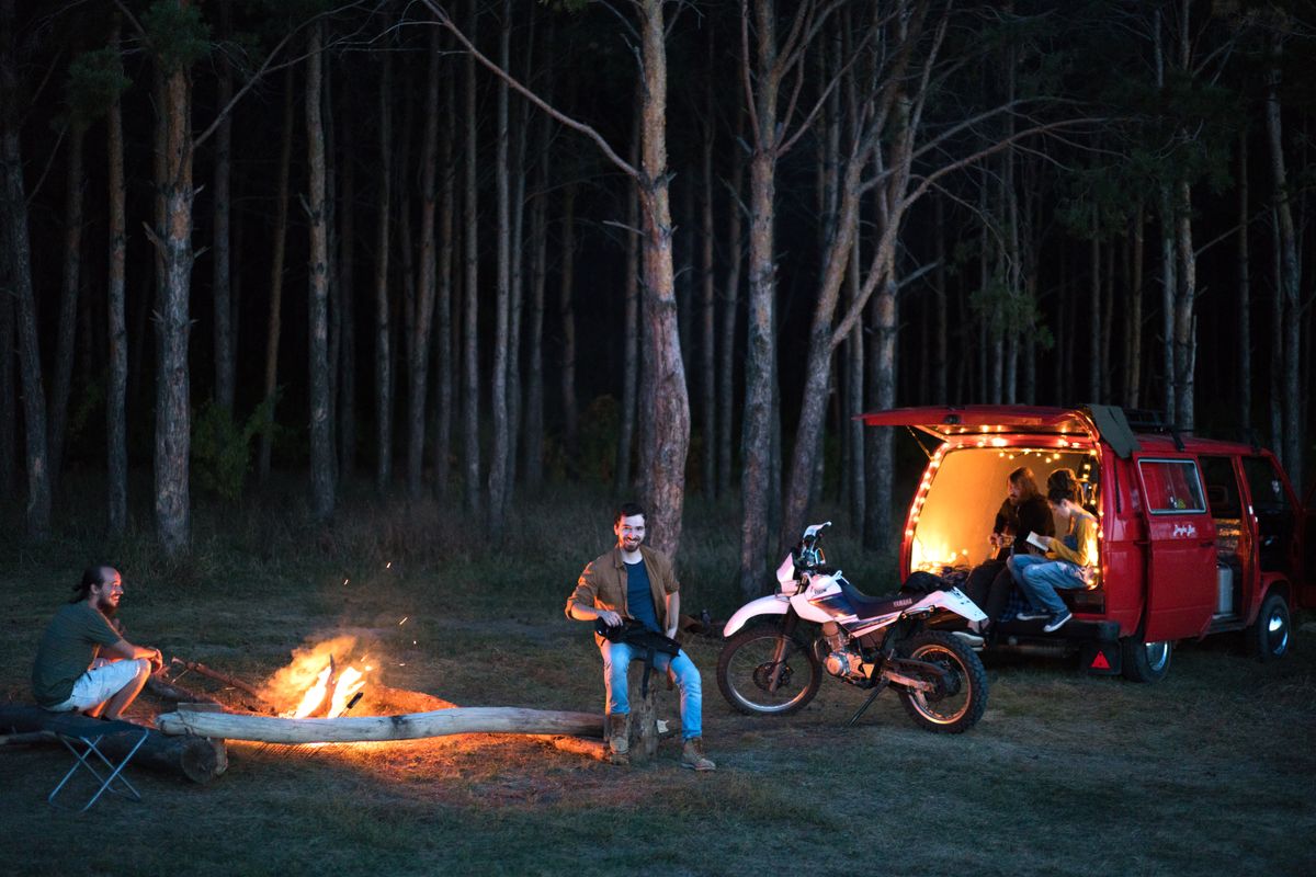 Group of friends enjoying a night camping with a bonfire, motorbike, and van.