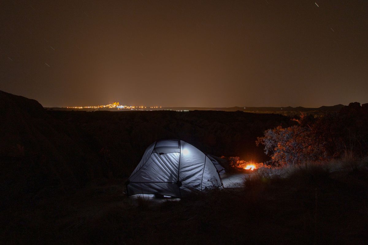 Serene camping scene under a starlit sky with city lights on the horizon.