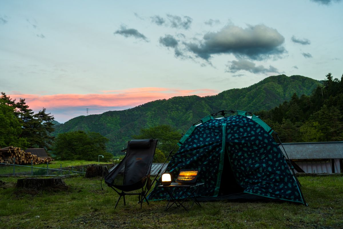 Serene camping setup with tent, chairs, and lantern against a picturesque mountain sunset.