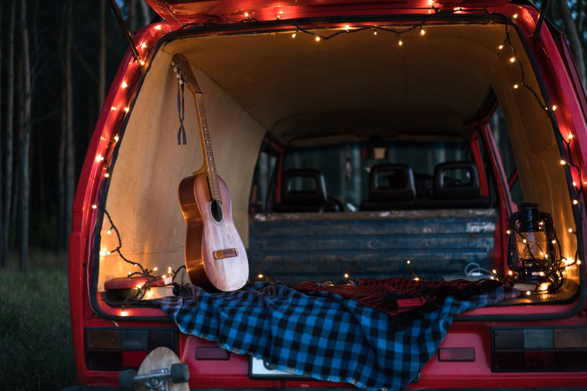 A serene camping scene with an acoustic guitar and lights in a car trunk, perfect for music lovers.