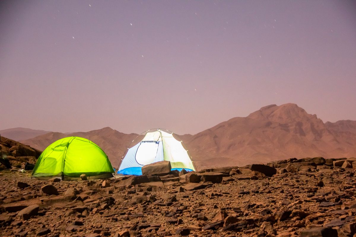 Night camping scene with tents under the stars in a rocky desert landscape.