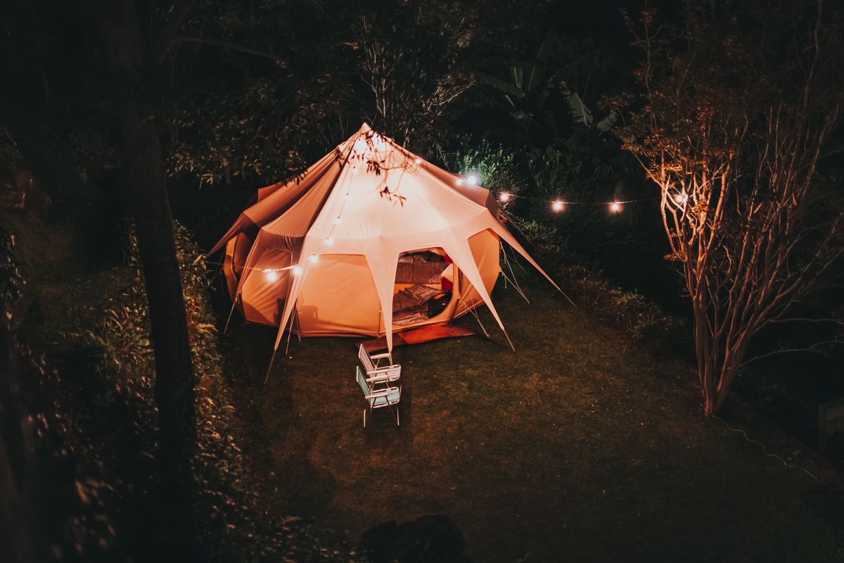 A cozy night camping scene with a glowing tent and string lights creating a warm ambiance.