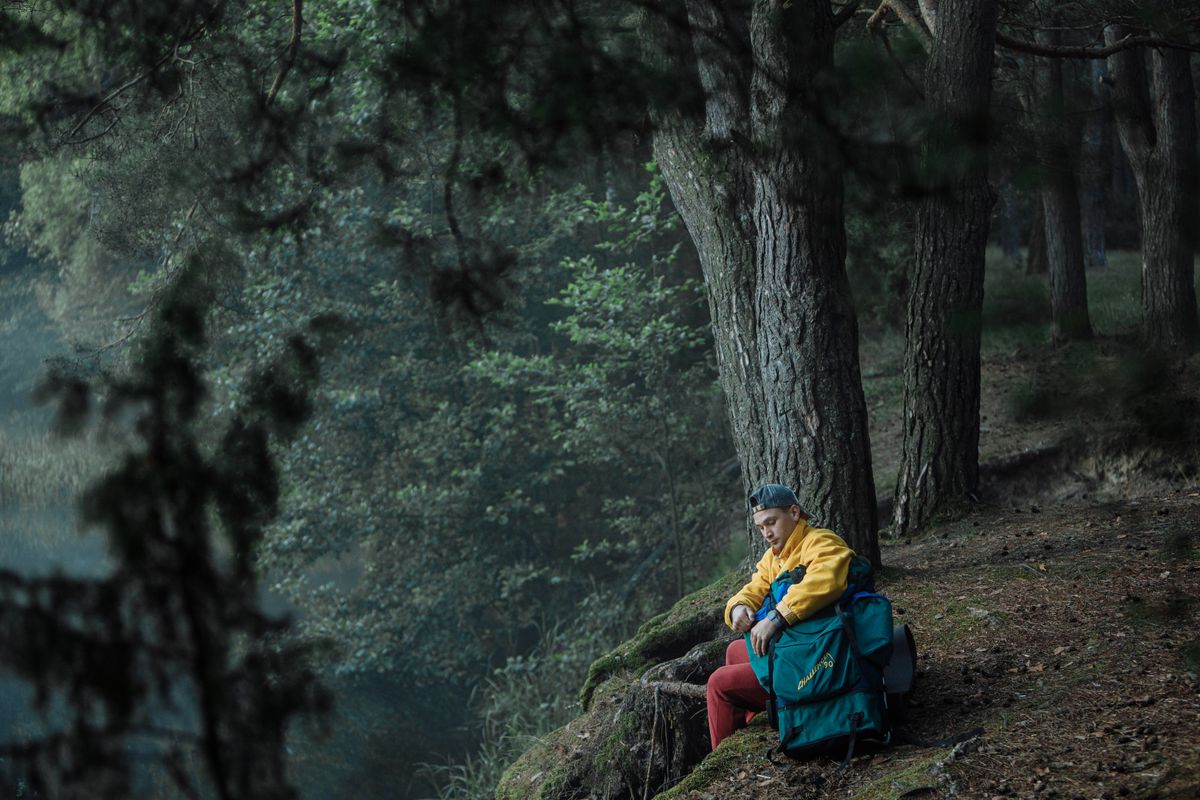 Man resting with backpack in serene forest, showcasing outdoor adventure and tranquility.