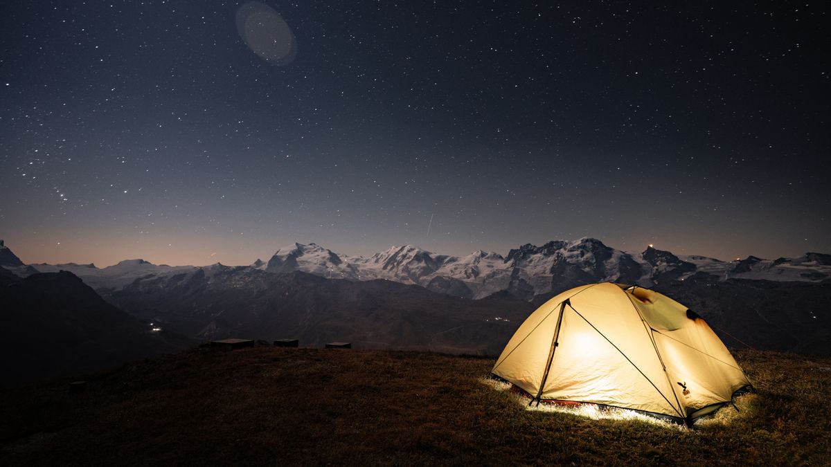 A tent illuminated under a starry night sky in Zermatt, surrounded by stunning mountain views.