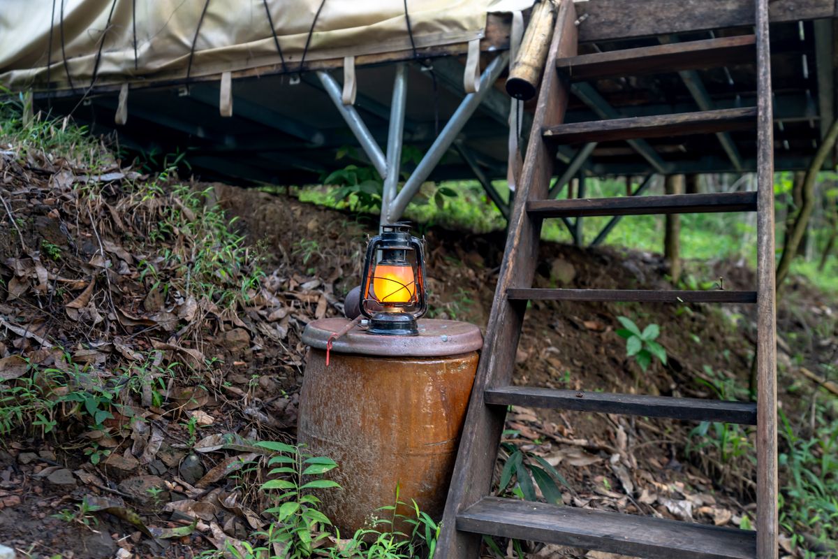 A rustic lantern glowing beside wooden stairs at an outdoor campsite setting.