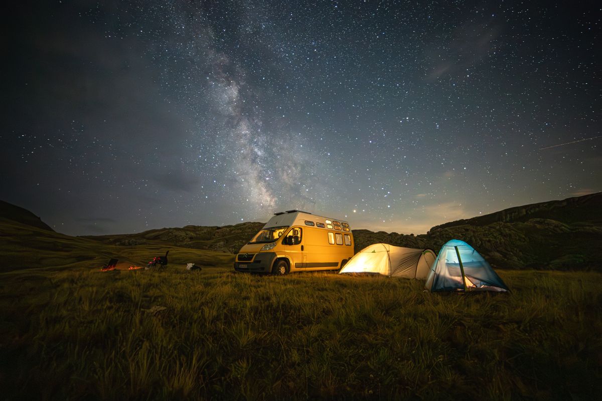 Experience the serenity of a starlit night camping in nature with a van and glowing tents.