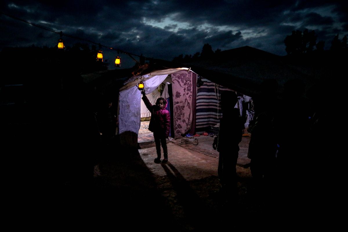 A child holding a lantern stands outside a tent under a dark sky in Idlib, Syria.