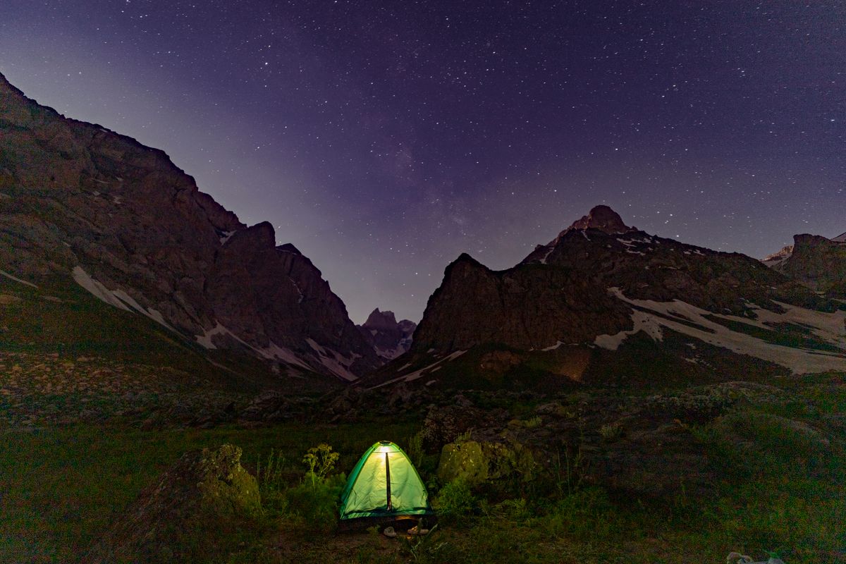 A glowing tent beneath starry mountain skies, perfect for night camping enthusiasts.