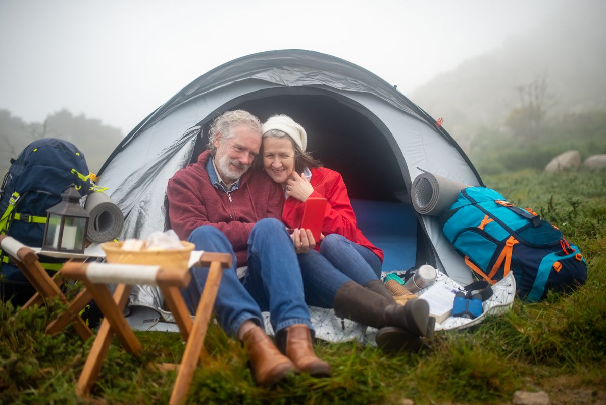 Senior couple relaxing in a tent amidst a foggy landscape, enjoying a cozy camping adventure.